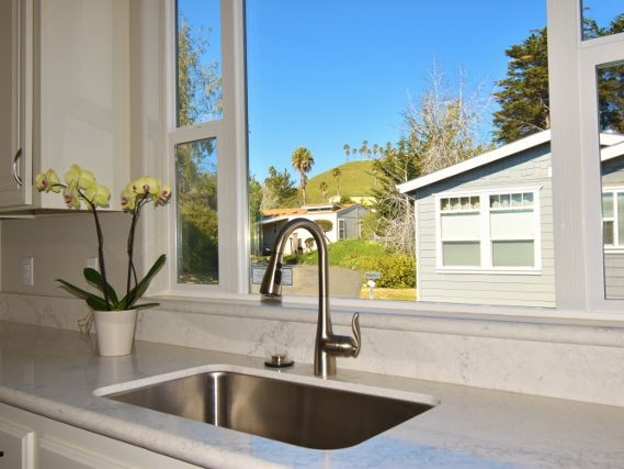 A white kitchen counter with stainless sink and a window at the back